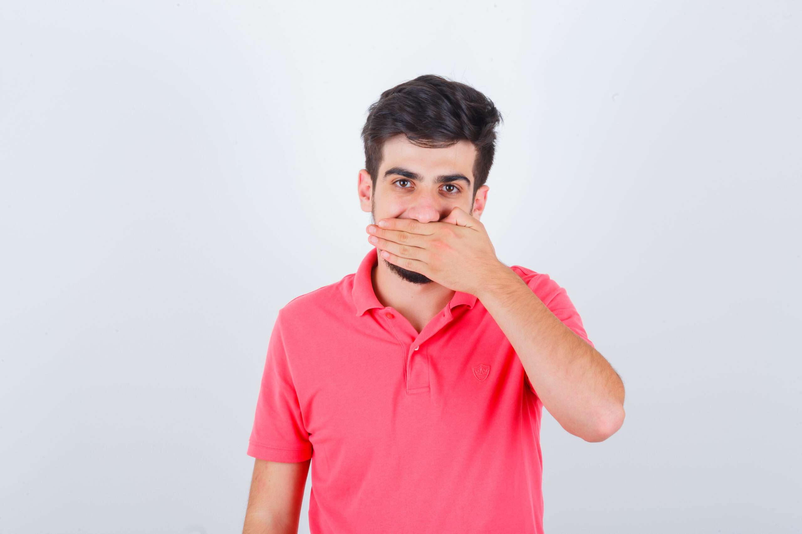 young male in pink t-shirt holding hand on mouth and looking merry , front view. Muh Ki Badbu Ka Ilaj