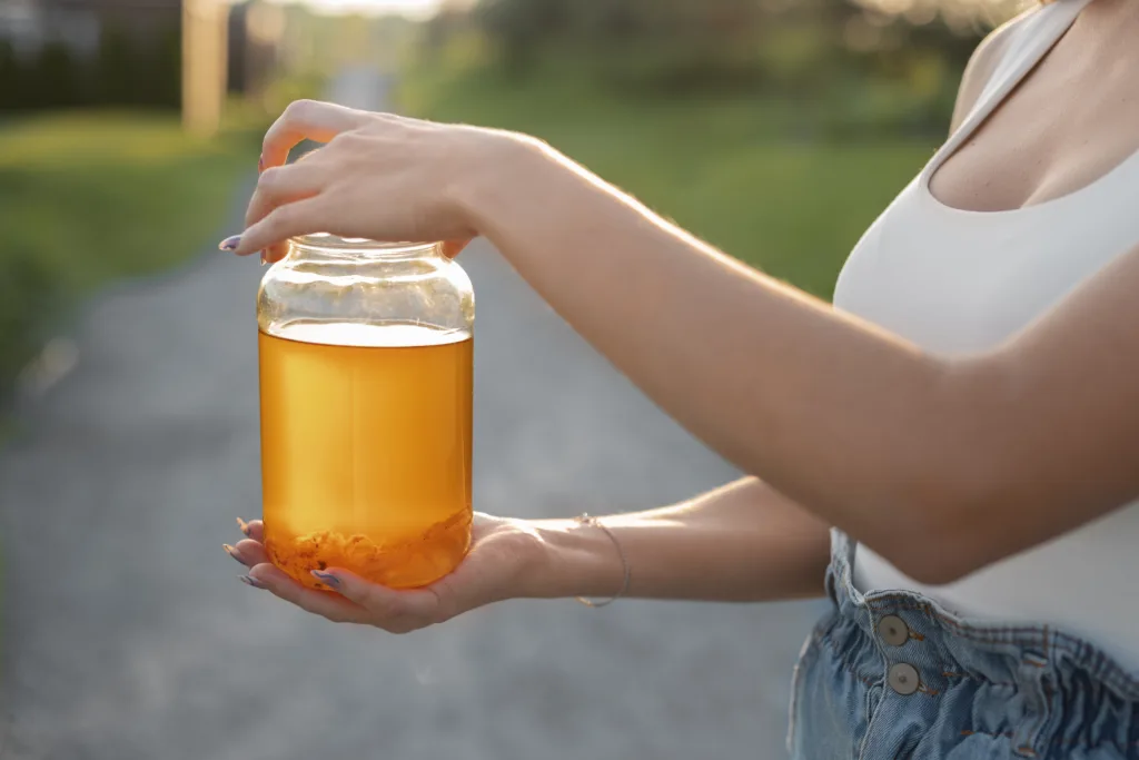 Woman holding a jar of kombucha – showcasing honey as natural remedies for allergies in kids by improving gut health.